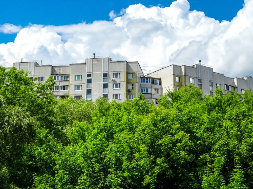 Multistory apartment buildings rising behind lush green trees under a clear blue sky