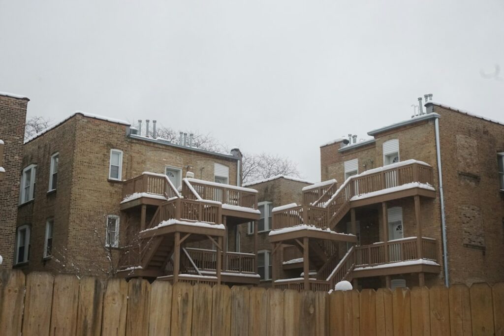 Low-rise brick apartment buildings with wooden balcony decks covered in fresh winter snow