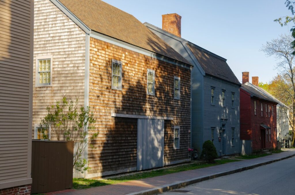 Row of older wooden multi-story houses lining a sunny residential street with long shadows
