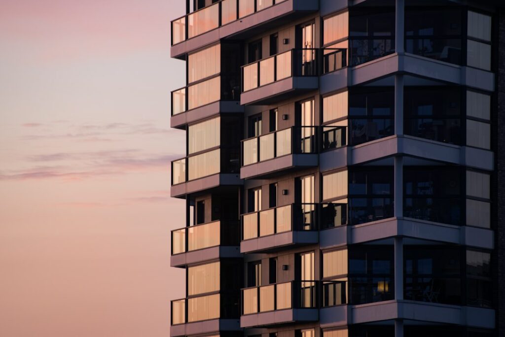Modern apartment building with glass balconies reflecting a soft pink evening sky