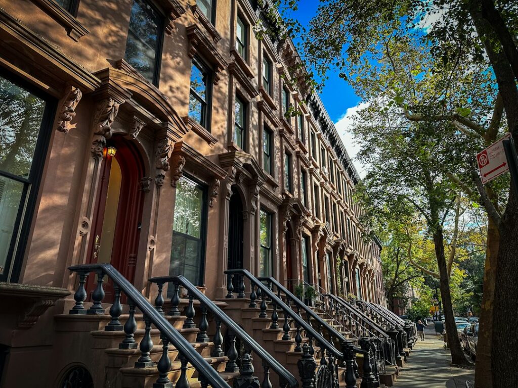 Row of attached brownstone residential buildings with front stoops lining a city street